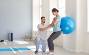 Woman performing a squat with a blue physioball with a trainer