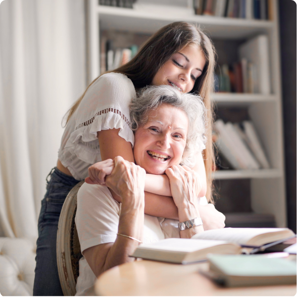 An elderly woman smiling and reading while her granddaughter hugs her