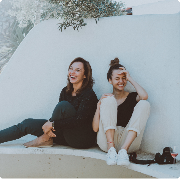 Two women sitting by a wall laughing