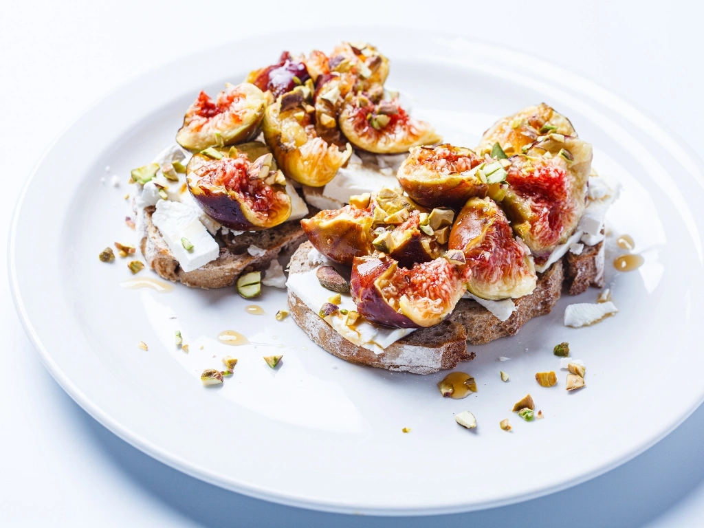 Ricotta sourdough toast with roasted figs and crushed pistachios on a white plate