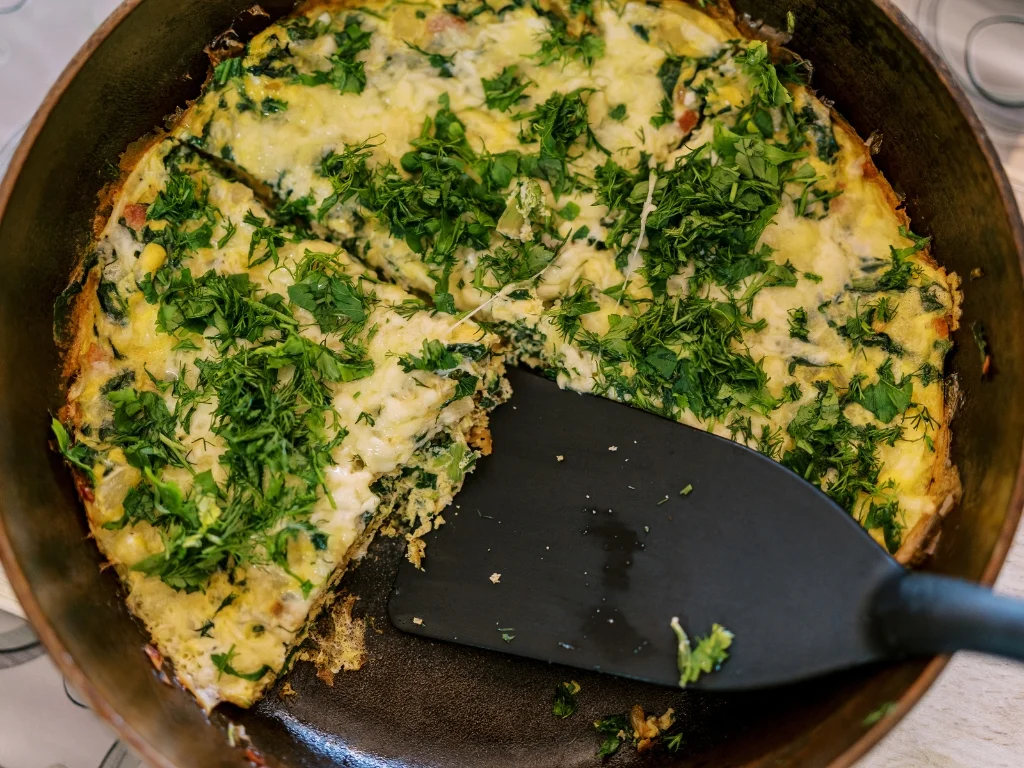 Sliced spinach and mushroom frittata in a pan with a black spatula