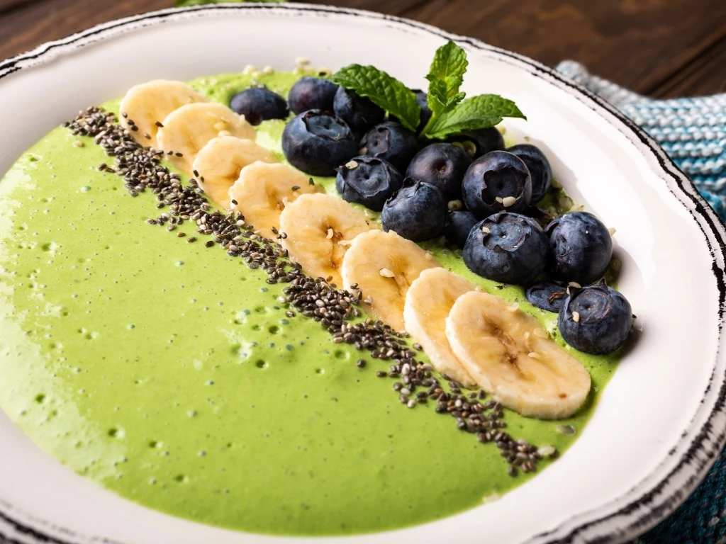 Bowl of green smoothie topped with banana slices, blueberries, chia seeds, and mint