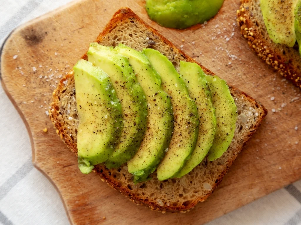 Whole-grain bread topped with avocado slices on a wooden board