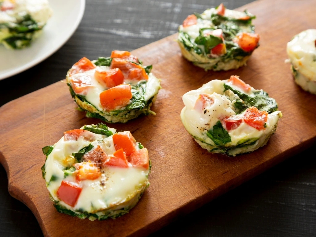 Egg white bites with spinach and tomatoes on a wooden board