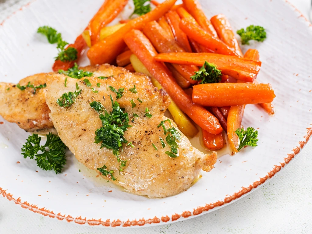 Plate of grilled chicken with steamed carrots seasoned with herbs