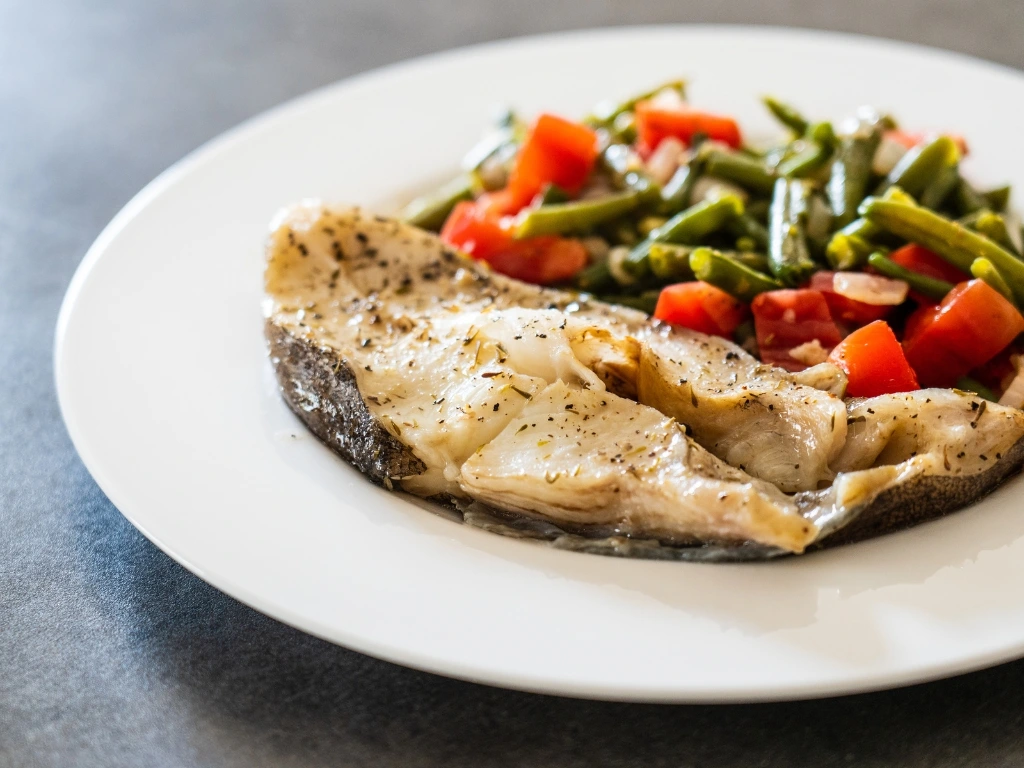Seasoned tilapia served on a white plate with a side of sautéed green beans and tomatoes