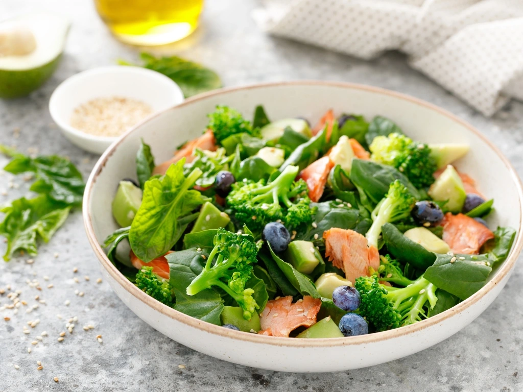 Vibrant salad bowl with fresh spinach, broccoli florets, flaked salmon, blueberries, and avocado topped with sesame seeds
