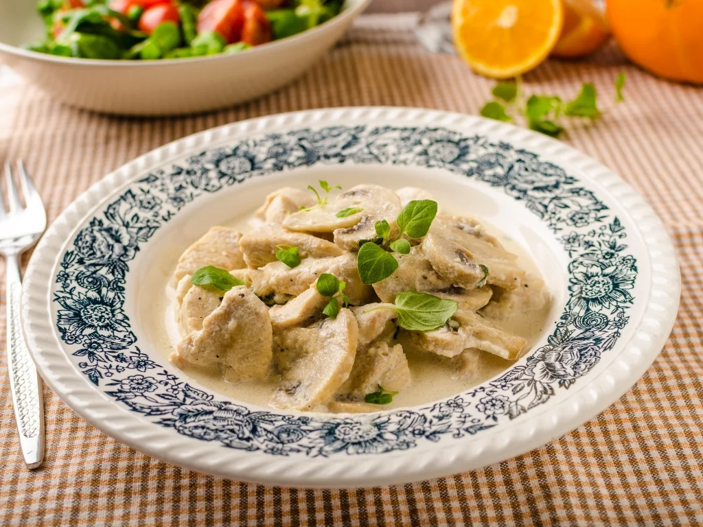Creamy chicken and mushroom fricassee served in a patterned white bowl, garnished with fresh green herbs