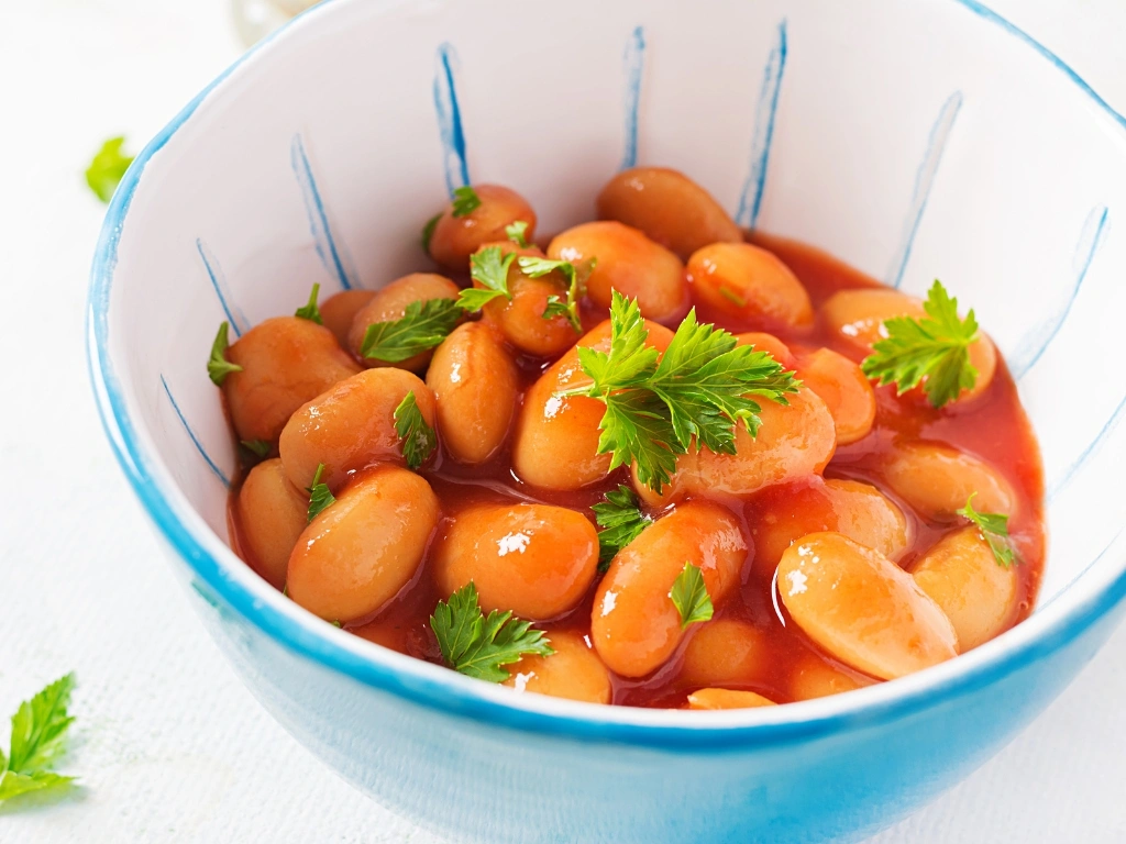 White bowl with blue stripes filled with large white beans in tomato sauce, garnished with fresh parsley