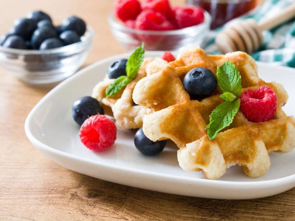 Whole-grain waffles topped with berries, served next to a jar of honey and small bowls of fruits