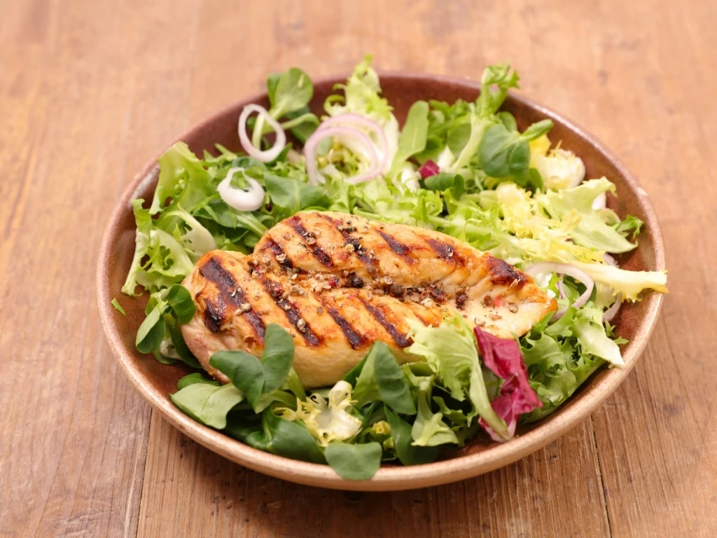 Plate of grilled chicken salad with mixed greens on a wooden table