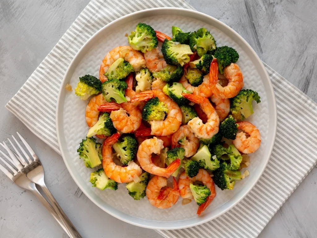 Plate of stir-fried shrimp and vegetables on a tablecloth, next to two forks