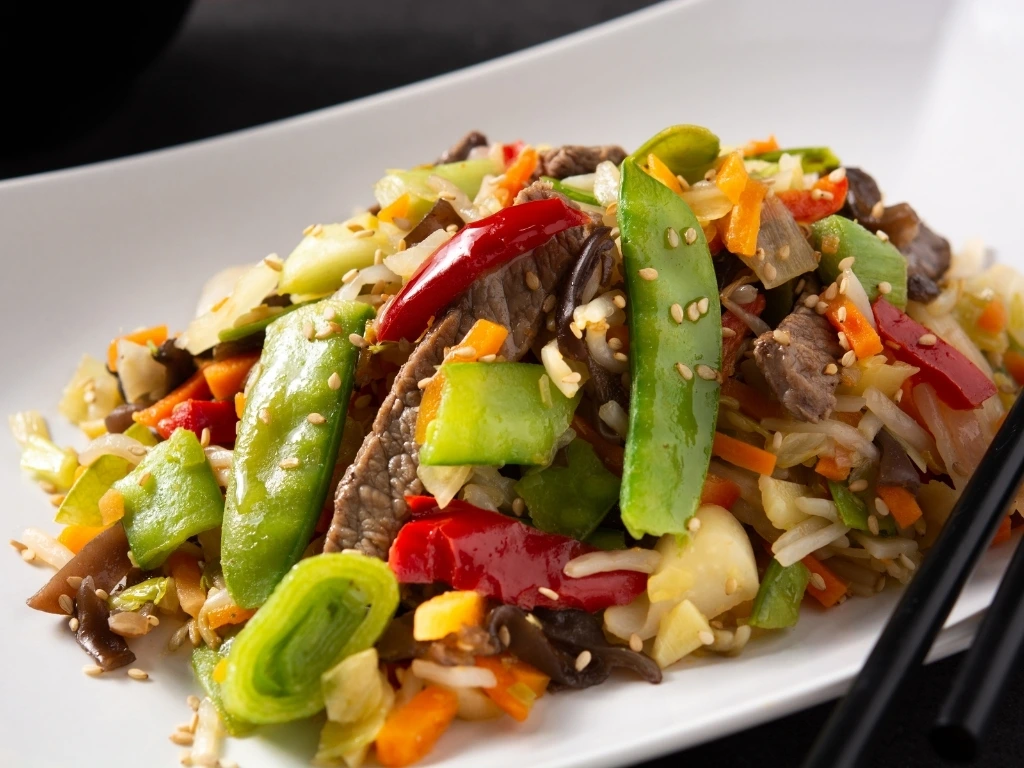 Beef and vegetable stir-fry served on a rectangular plate with a pair of chopsticks