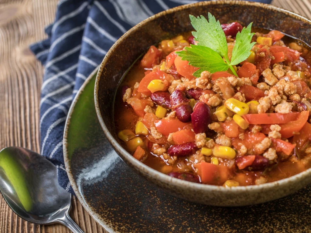 Bowl of turkey chili with kidney beans, corn, and tomatoes, garnished with a fresh sprig of parsley