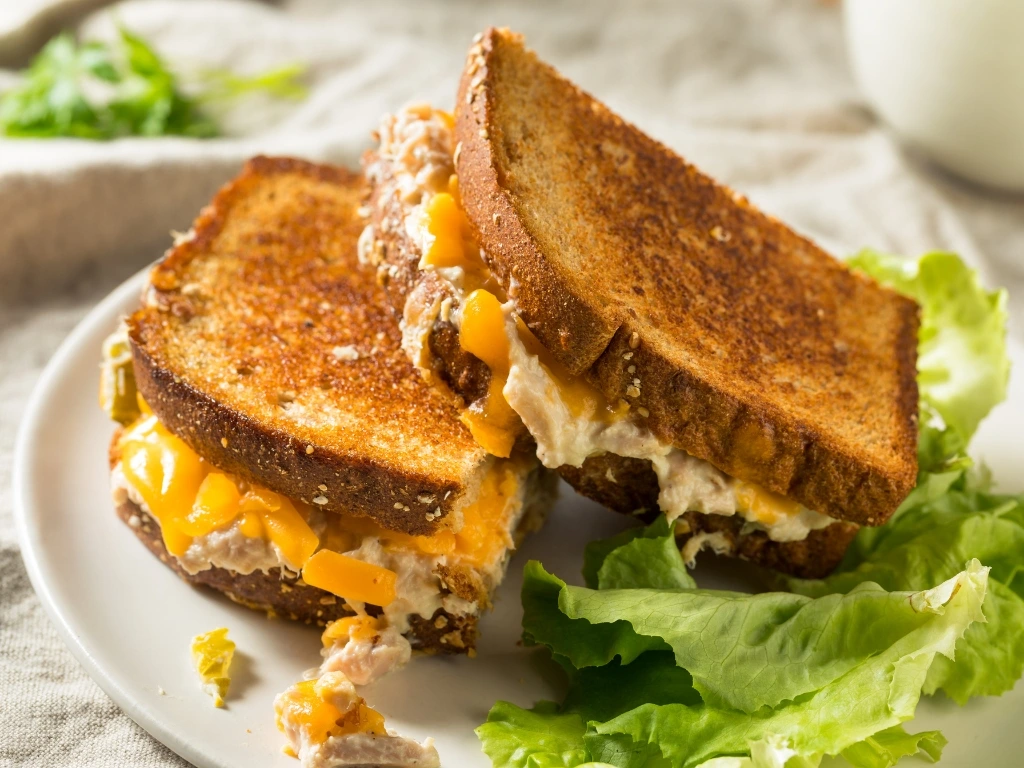 Toasted tuna melt sandwich with melted cheddar cheese on whole grain bread