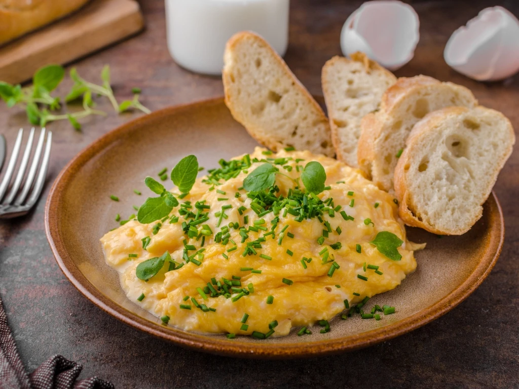Plate of scrambled eggs topped with herbs, served with sliced bread