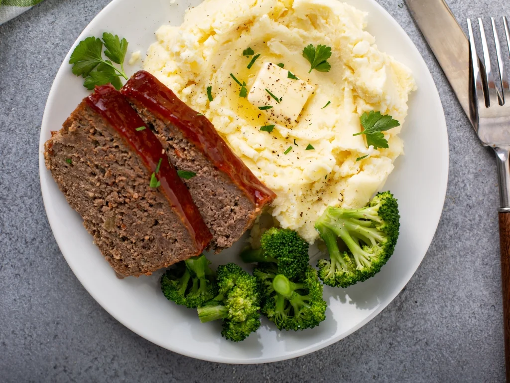 Slices of turkey meatloaf served with mashed potatoes, green beans, broccoli, and greens on a white plate
