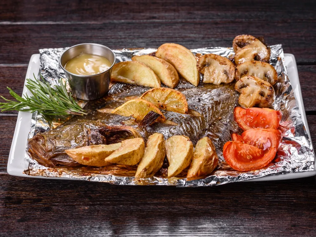 Baked whole fish served on a rectangular plate with roasted potatoes, mushrooms, and tomatoes