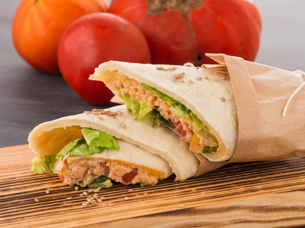 Two tuna salad wrap halves on a wooden board with whole tomatoes in the background