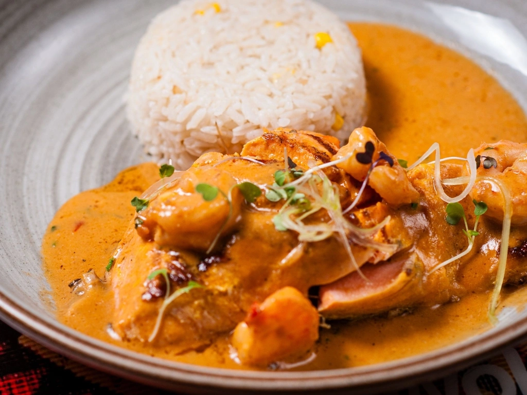 Plate of grilled salmon and shrimp covered in creamy orange sauce with a side of white rice