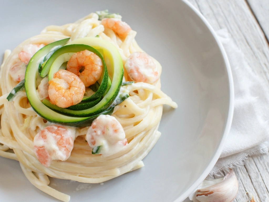Plate of creamy shrimp pasta topped with sliced zucchini ribbons