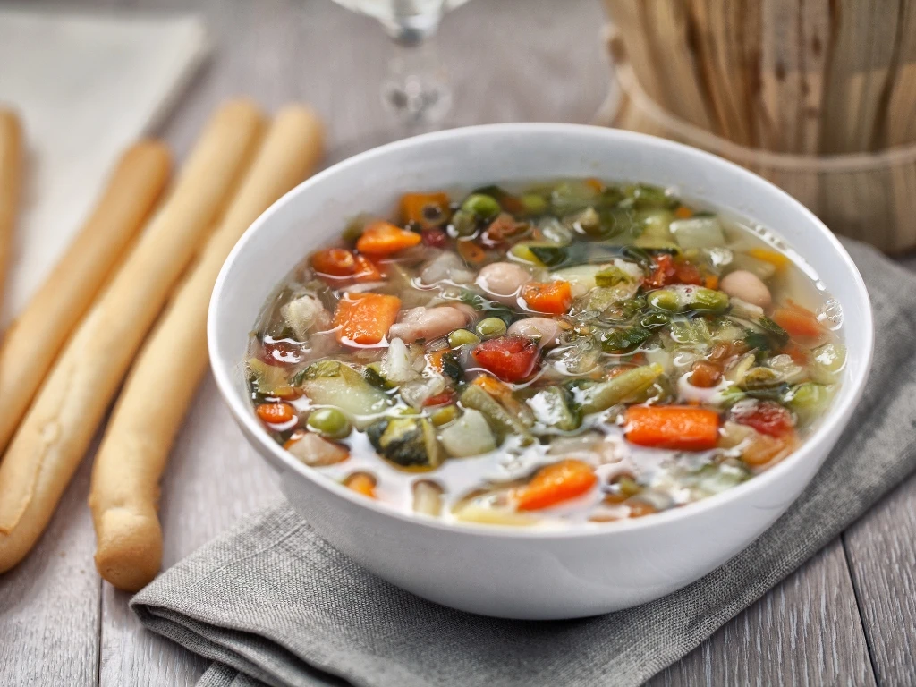 White bean and vegetable soup served next to four breadsticks on a wooden table