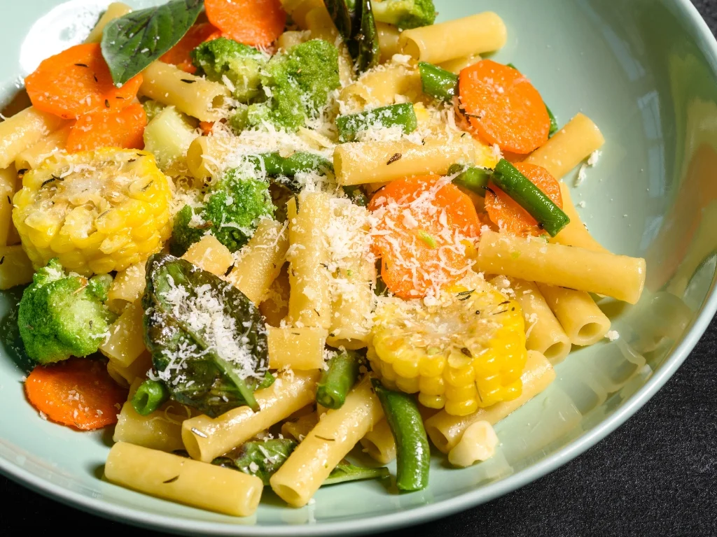 Pasta primavera with beans and roasted vegetables, served on a blue plate
