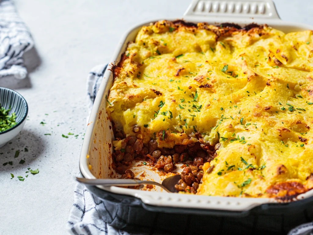 Vegan shepherd's pie in a ceramic baking dish, next to a small bowl of fresh herbs