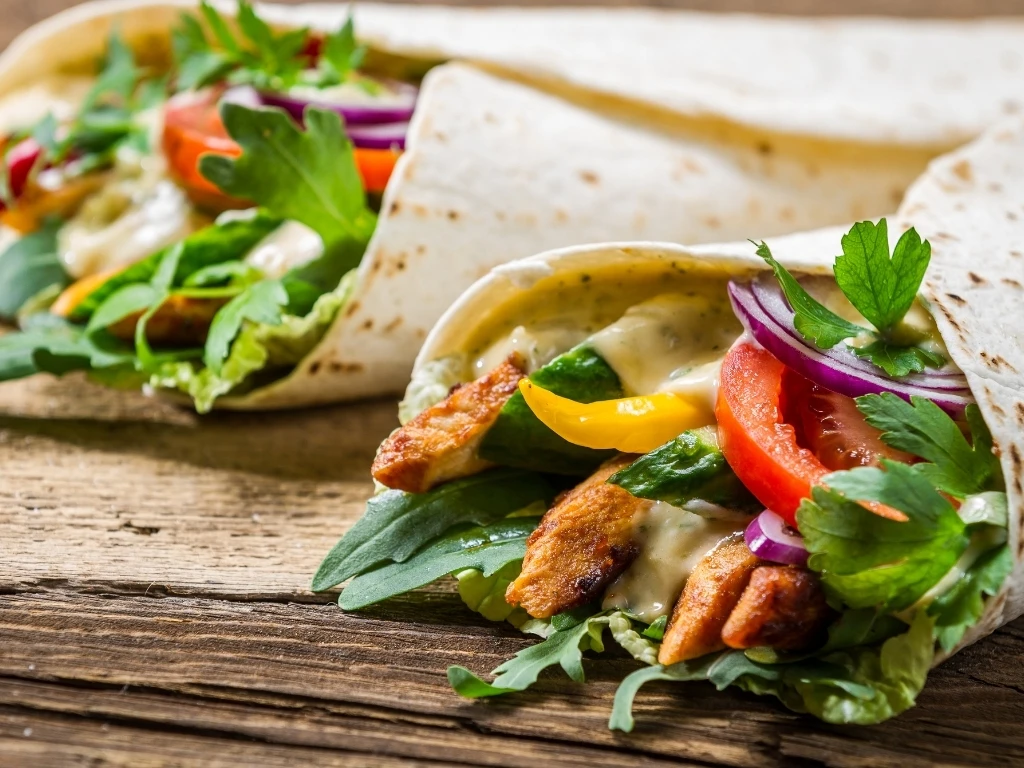 Two whole-wheat wraps with grilled chicken and vegetables on a wooden board