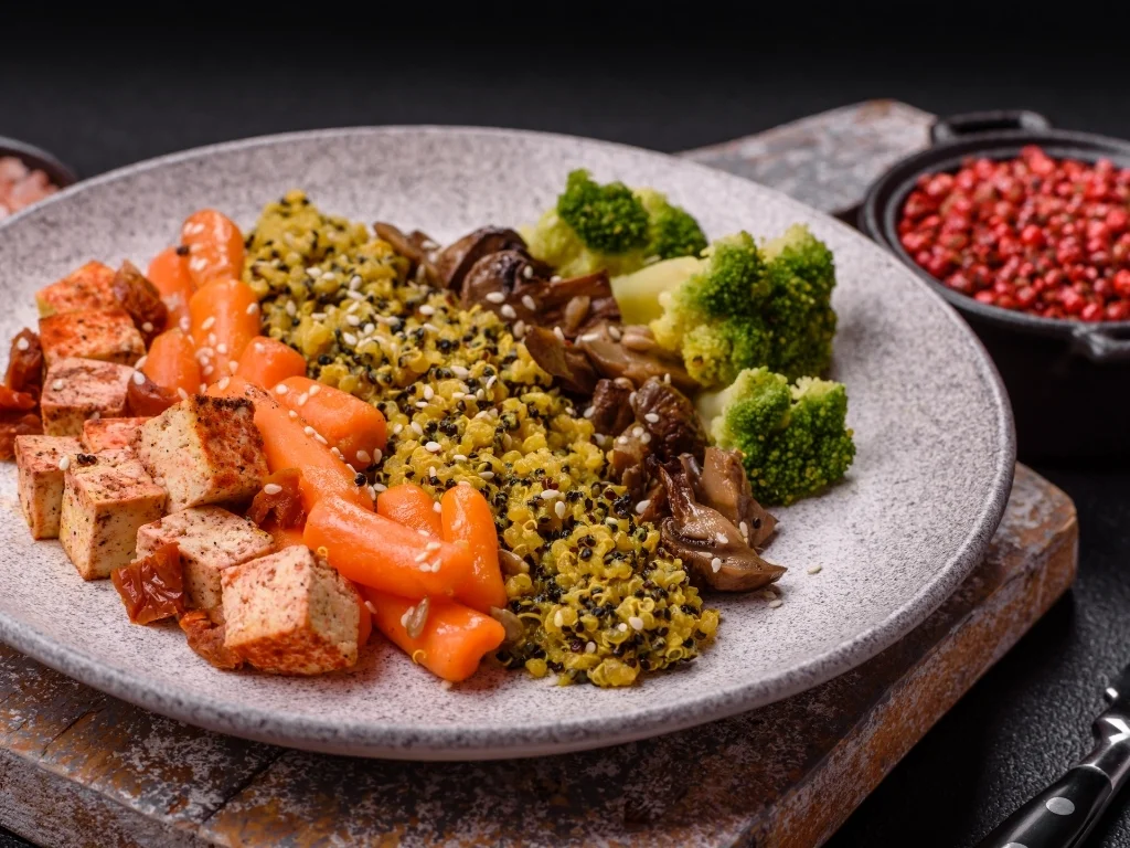 Plate of seasoned tofu, quinoa with sesame seeds, roasted carrots, steamed broccoli, and sautéed mushrooms