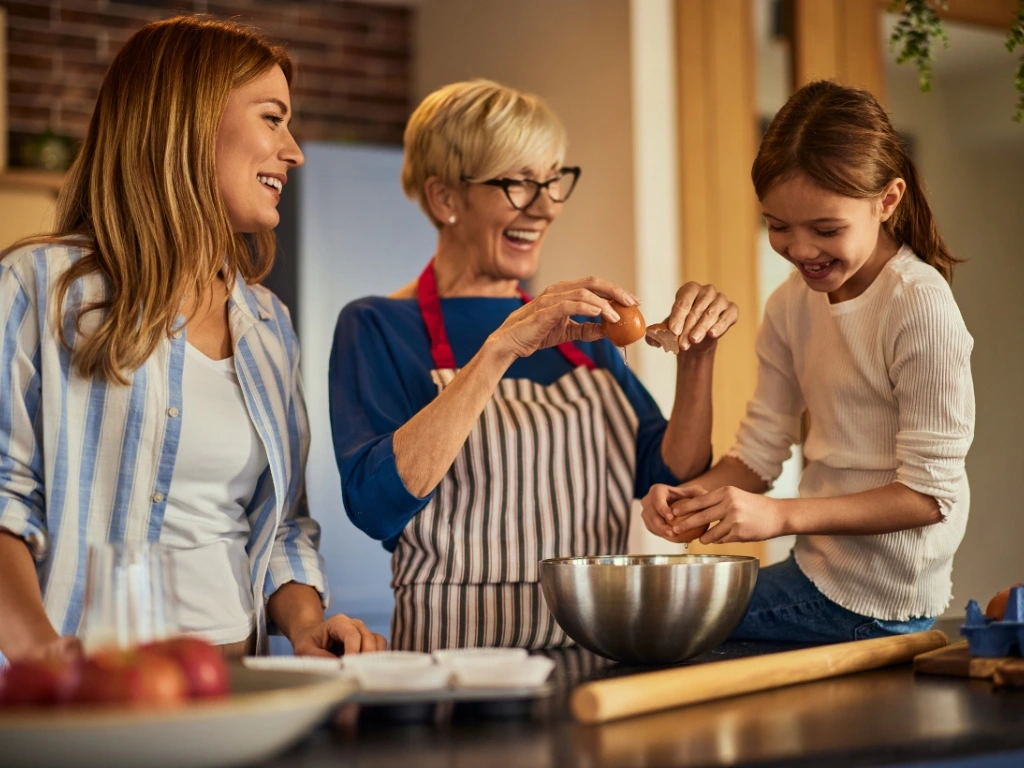 Parents and a child happily preparing food in the kitchen, cracking eggs into a silver mixing bowl