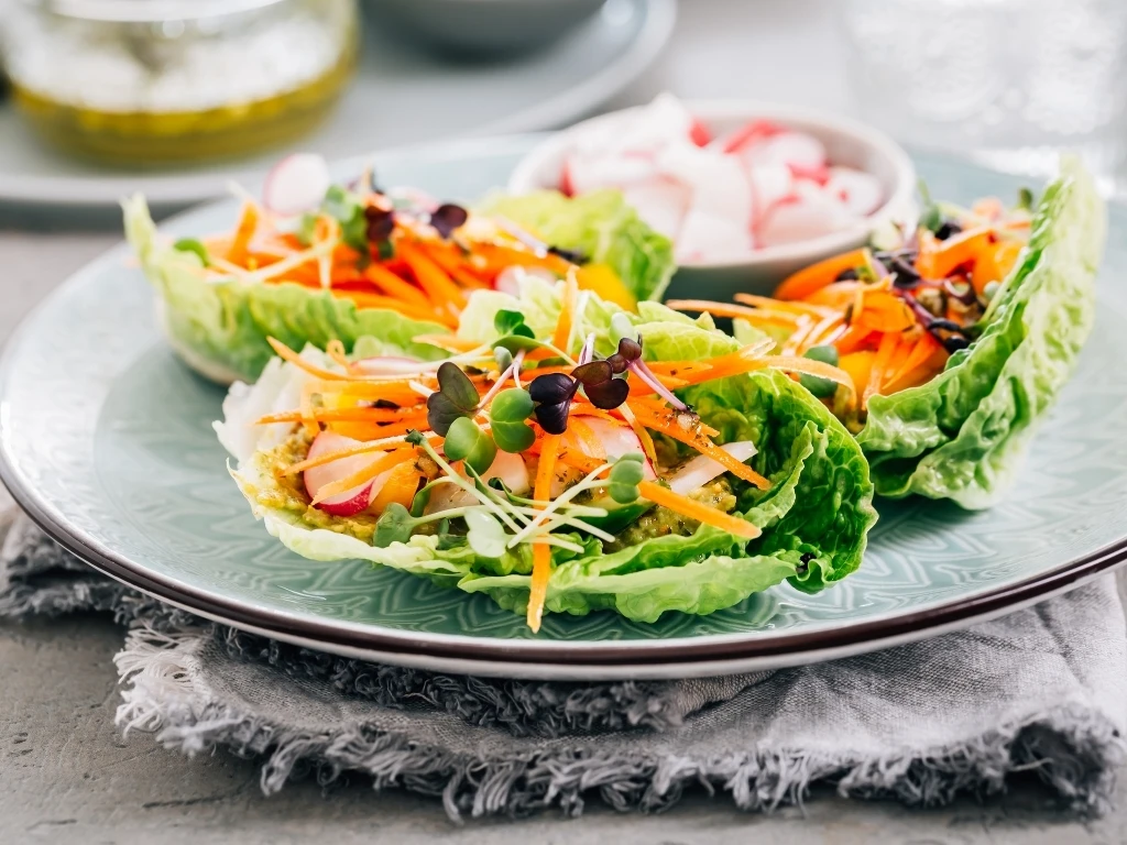 A plate of turkey lettuce wraps with shredded carrots and fresh herbs