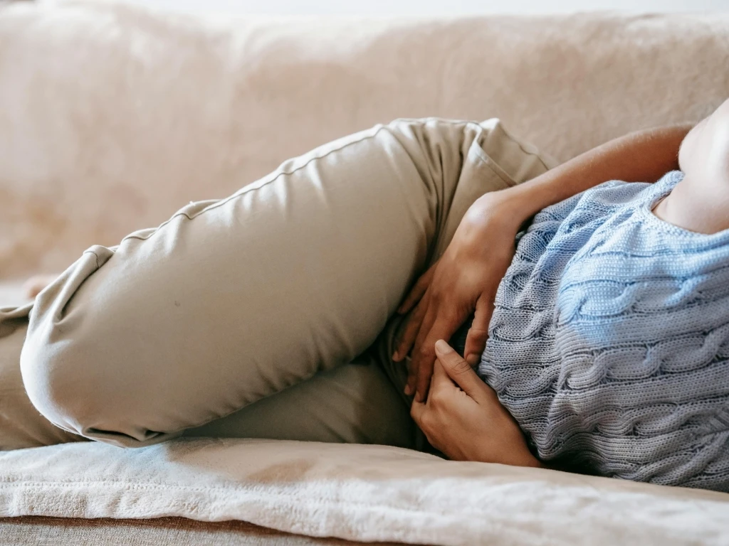 Person resting on a couch, holding their abdomen in pain
