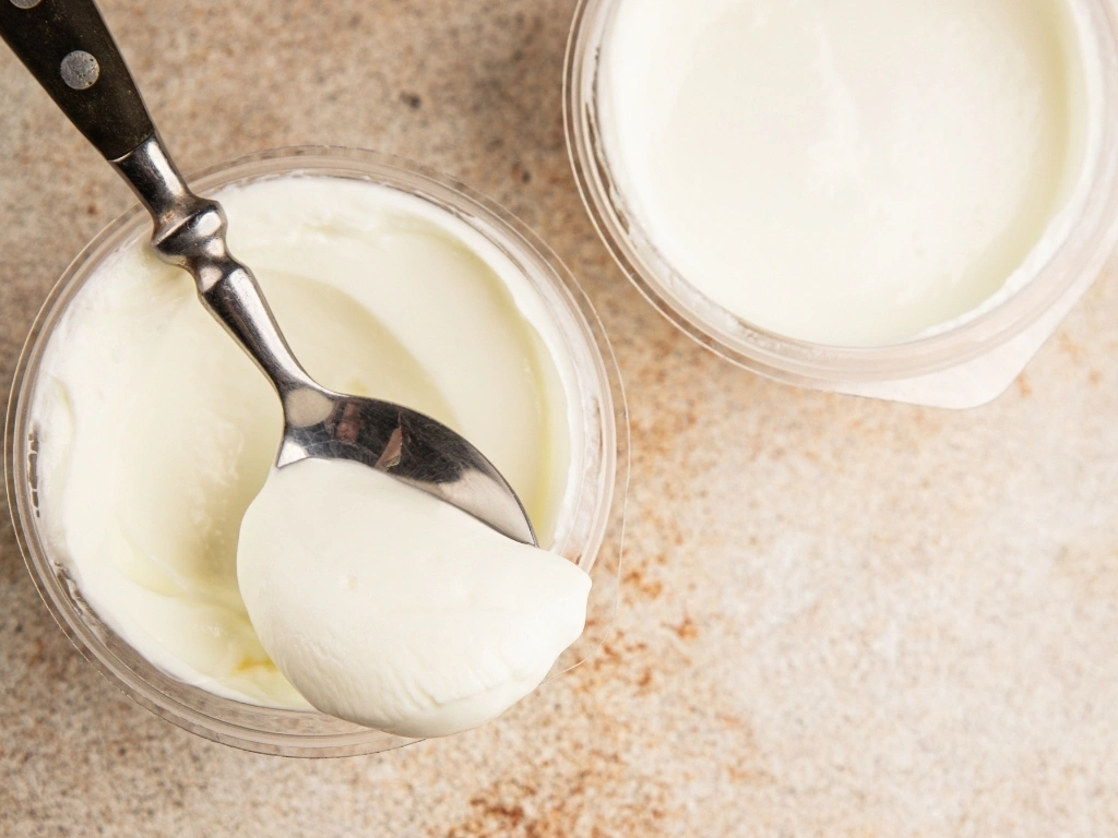 Two yogurt cups, with a spoon scooping from the leftmost cup