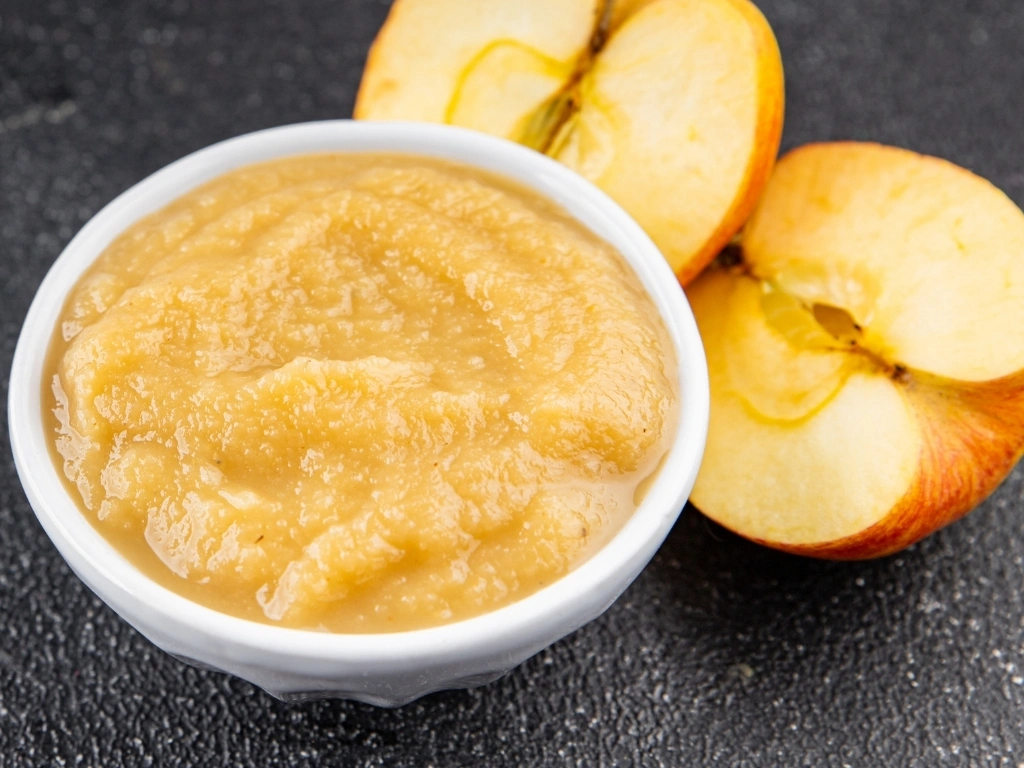 Bowl of applesauce next to sliced apples