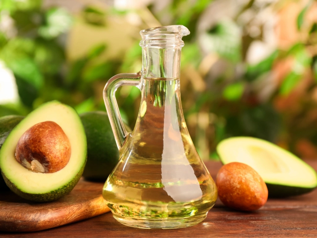 Jug of olive oil and sliced avocados on a wooden table