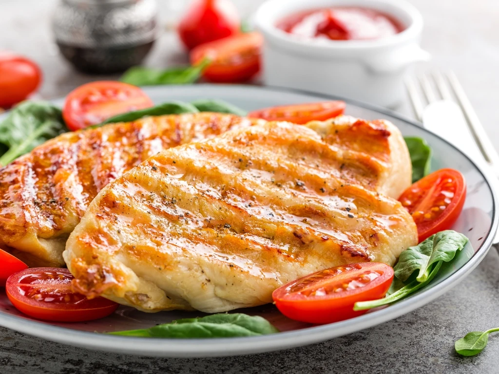 Grilled chicken breast served with sliced tomatoes and leafy greens