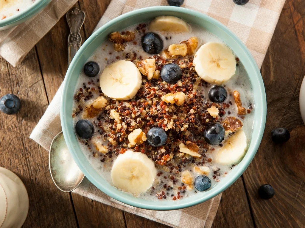 Bowl of crispy quinoa yogurt bowl served with banana slices and blueberries, served next to a spoon on a tablecloth