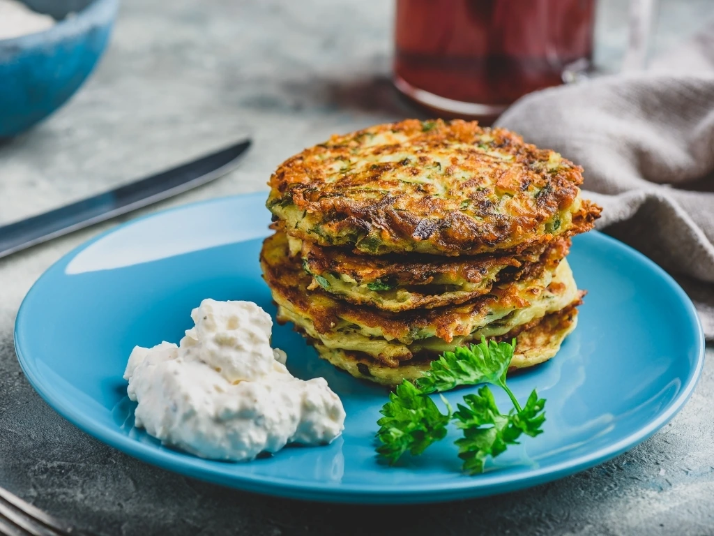 Veggie chickpea fritters served on a blue plate with a yogurt-based dip and garnished with herbs