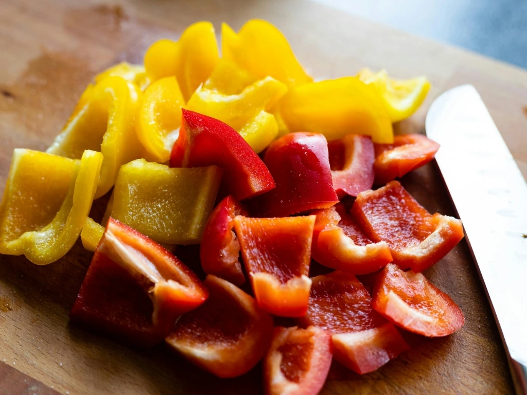Sliced yellow and red bell peppers on a wooden board next to a knife