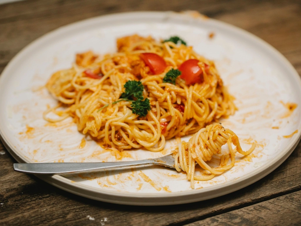 Partially eaten plate of spaghetti with tomato sauce and cherry tomatoes