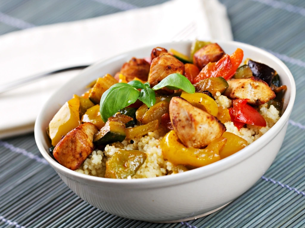 Bowl of seasoned couscous topped with stir-fried chicken and bell peppers, garnished with green onions