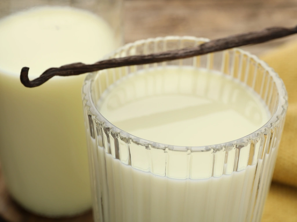 Two glasses of soy milk with vanilla bean across the rim of one glass