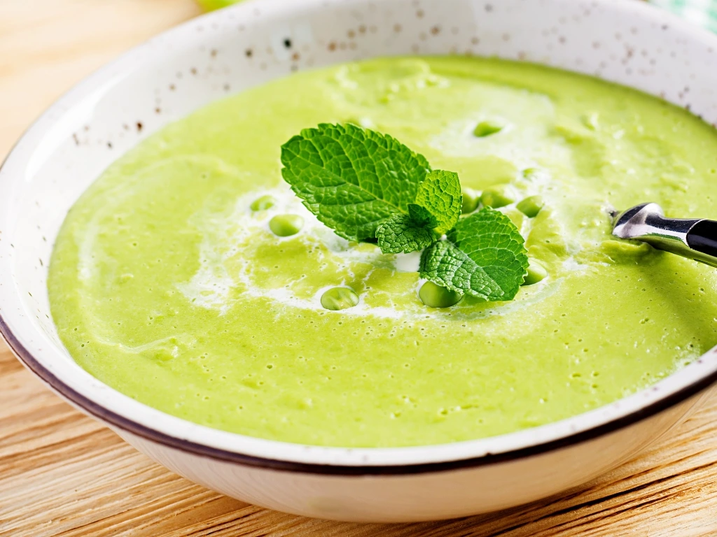 Green pea soup in a bowl, garnished with herbs
