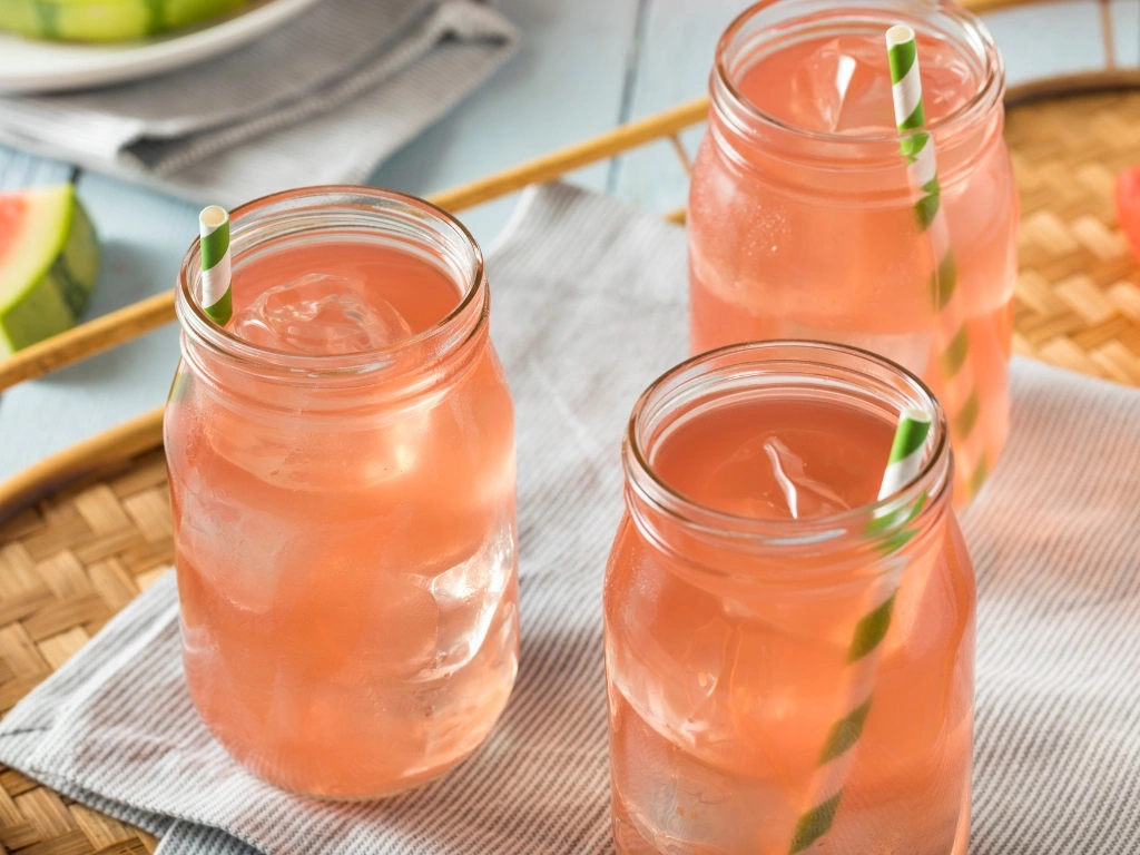 Three glasses of iced watermelon juice, served with straws and tablecloth on a wooden table