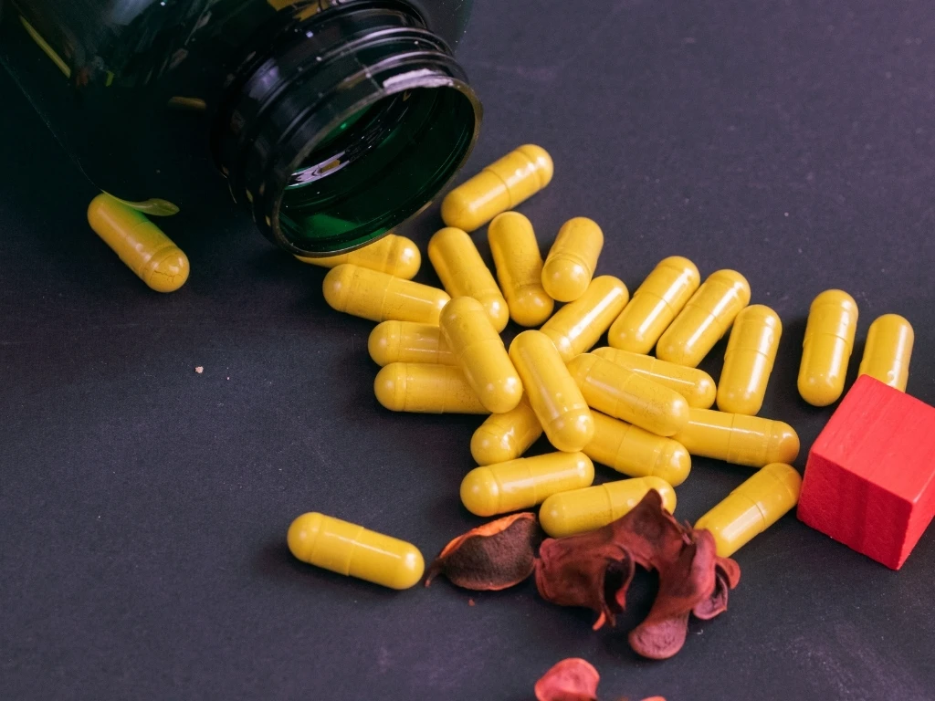 Green bottle of supplements with yellow capsules on a black background