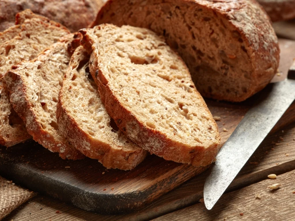 Sliced whole wheat bread on a wooden board next to a bread knife