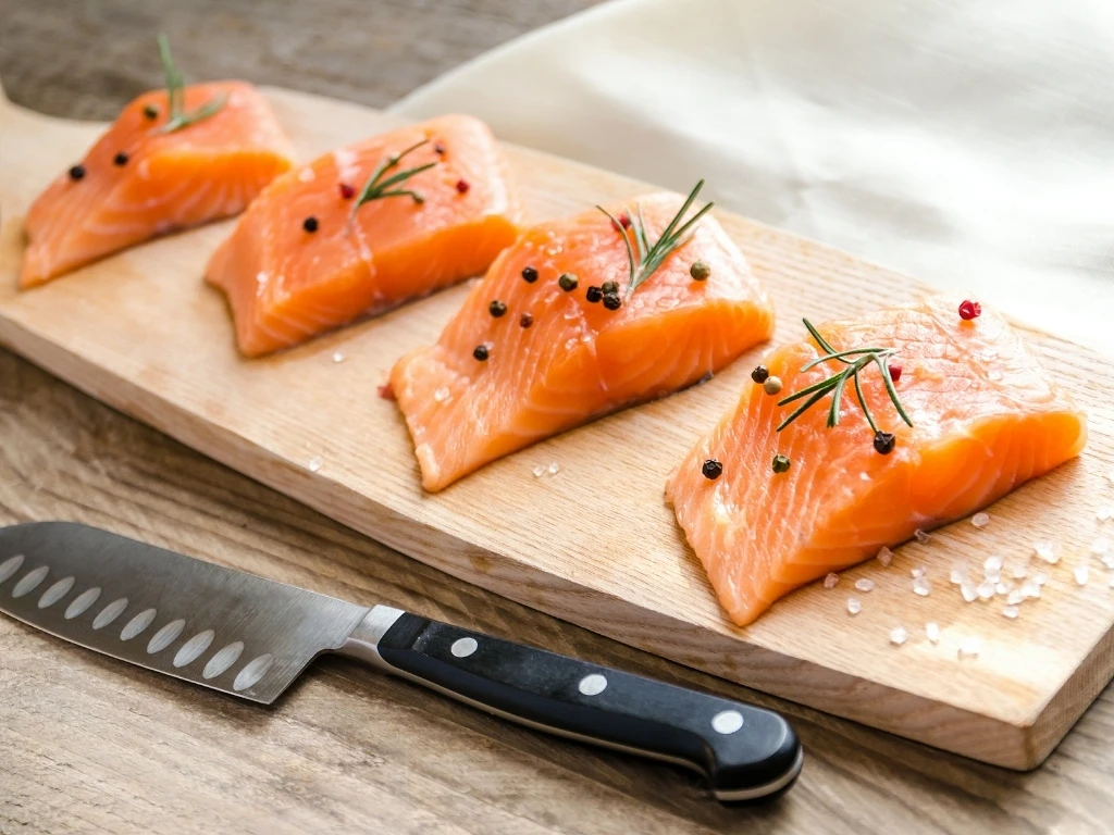 Slices of salmon on a wooden tray next to a kitchen knife 