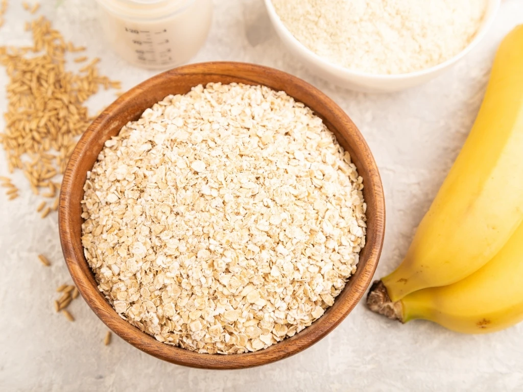 Uncooked oats in a wooden bowl surrounded by unpeeled bananas