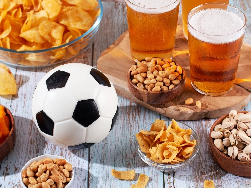 Beer in glasses and snack on wooden table with football ball, football game night food